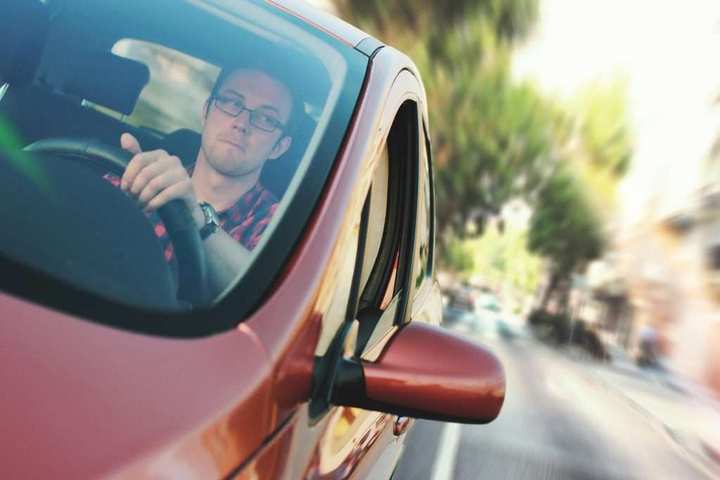 Man driving car, viewed through side mirror