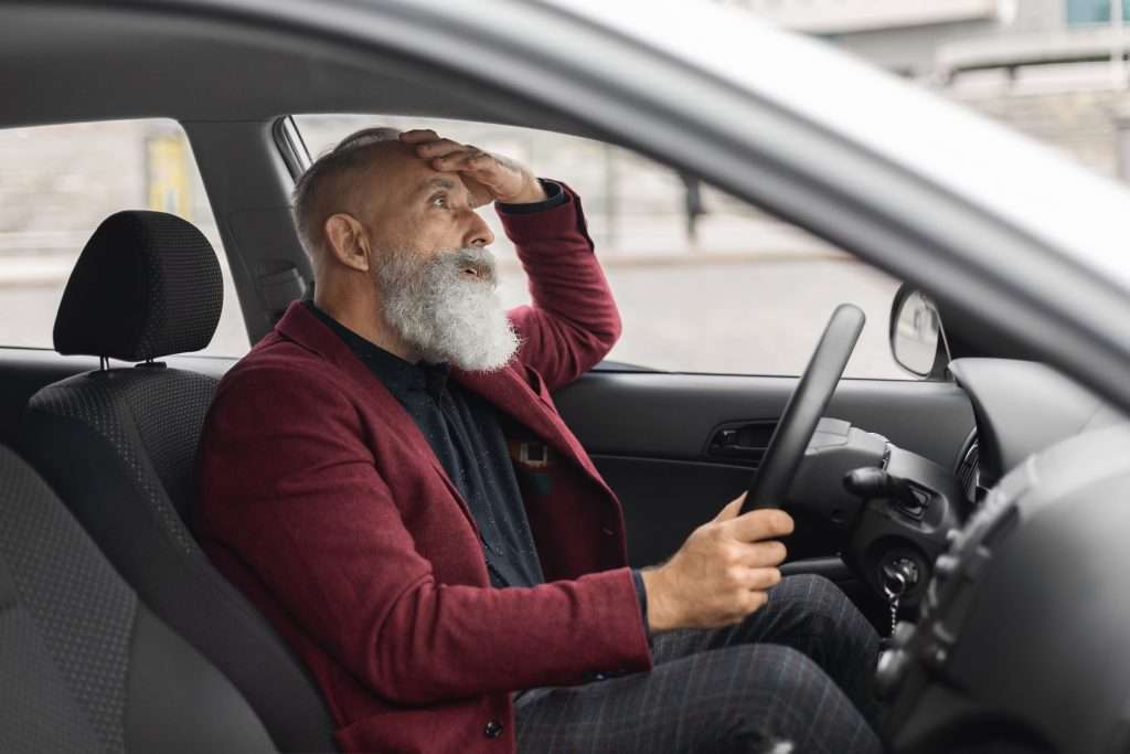 Stressed senior man driving car, looking worried