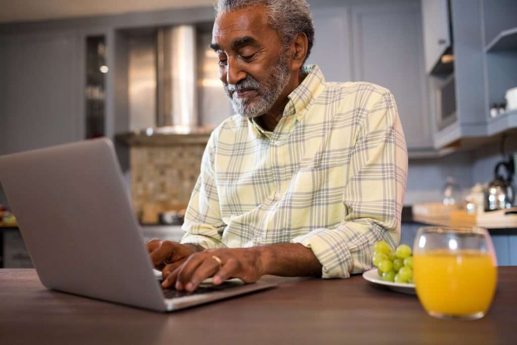 Senior man using laptop in kitchen with juice and grapes